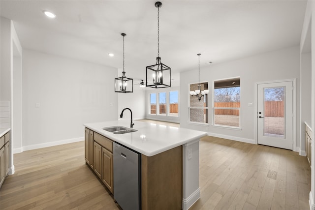 kitchen featuring light hardwood / wood-style floors, stainless steel dishwasher, sink, decorative light fixtures, and an island with sink