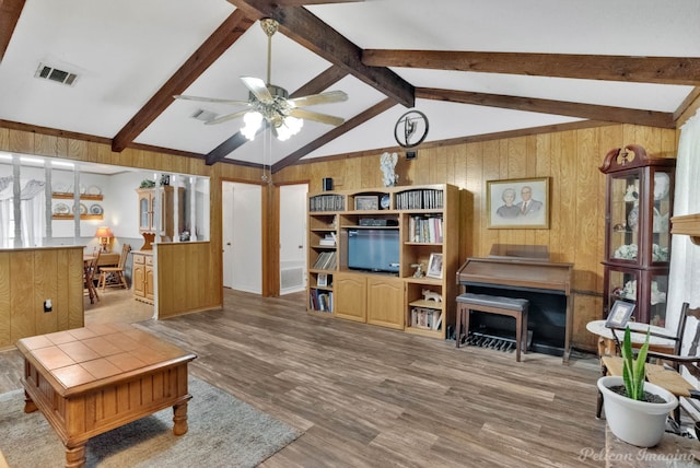 living room featuring hardwood / wood-style flooring, vaulted ceiling with beams, wood walls, and ceiling fan