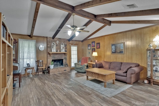 living room with ceiling fan, a brick fireplace, lofted ceiling with beams, wood walls, and wood-type flooring