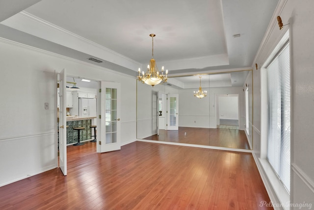 unfurnished dining area with french doors, an inviting chandelier, hardwood / wood-style floors, a tray ceiling, and ornamental molding