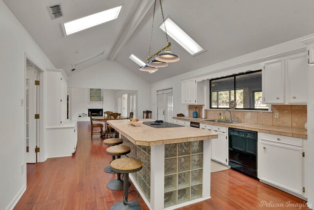 kitchen featuring sink, lofted ceiling with skylight, white cabinets, black appliances, and light wood-type flooring