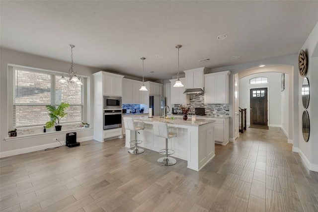 kitchen with exhaust hood, white cabinetry, an island with sink, and stainless steel appliances