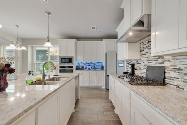 kitchen with sink, wall chimney exhaust hood, appliances with stainless steel finishes, tasteful backsplash, and light stone counters