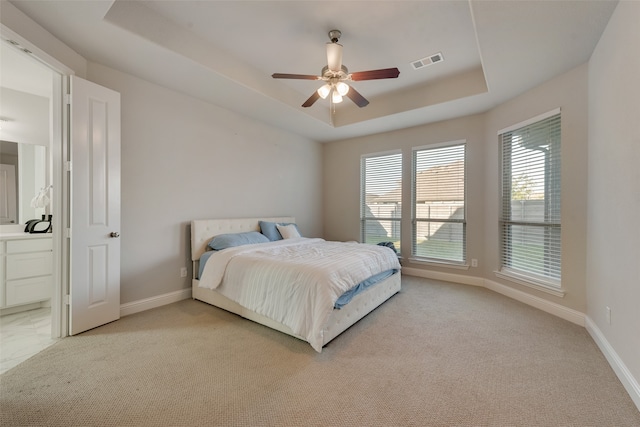 carpeted bedroom with connected bathroom, a tray ceiling, and ceiling fan