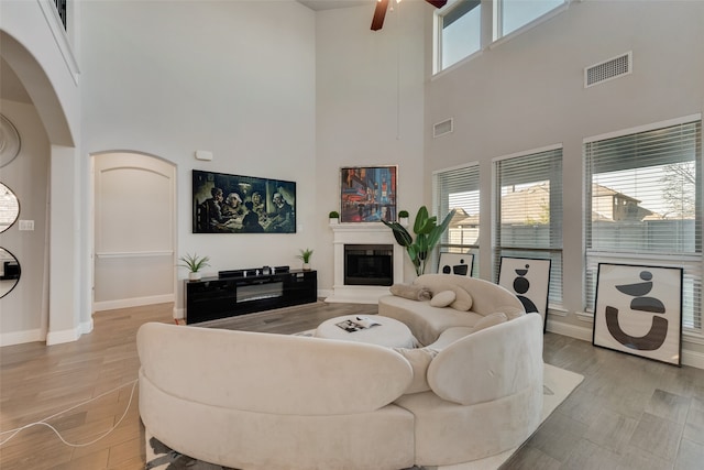 living room featuring ceiling fan, light hardwood / wood-style floors, and a towering ceiling