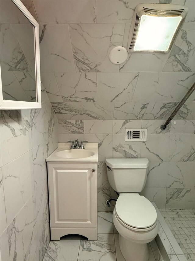 bathroom featuring walk in shower, vanity, tile walls, and toilet