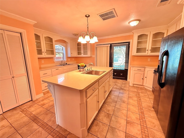 kitchen featuring pendant lighting, black refrigerator with ice dispenser, white cabinets, sink, and an island with sink