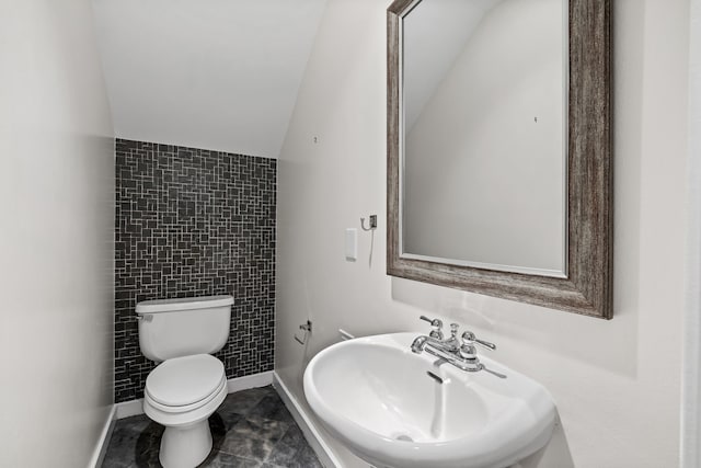 bathroom featuring sink, tile patterned floors, lofted ceiling, toilet, and tile walls