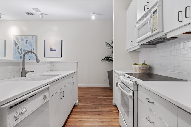 kitchen with white appliances, sink, tasteful backsplash, light hardwood / wood-style floors, and white cabinetry