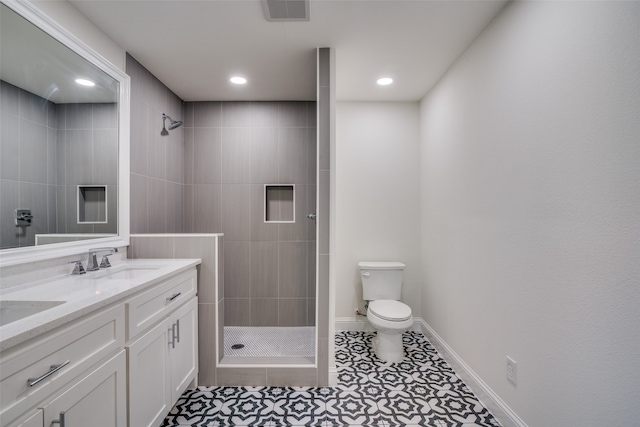 bathroom featuring tile patterned flooring, a tile shower, vanity, and toilet