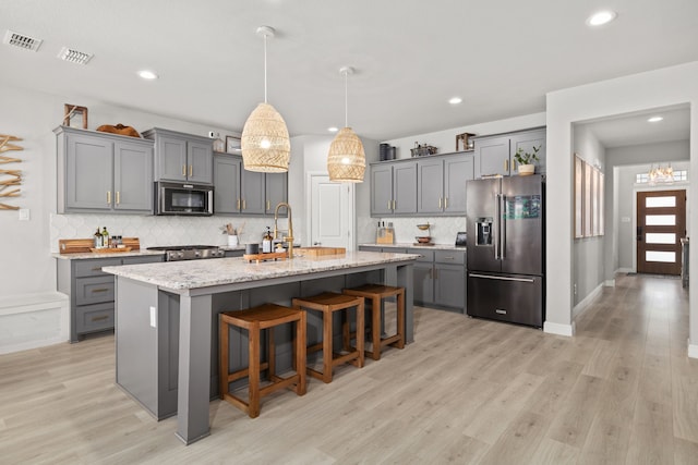 kitchen featuring light stone counters, light hardwood / wood-style floors, a kitchen island with sink, a breakfast bar, and appliances with stainless steel finishes