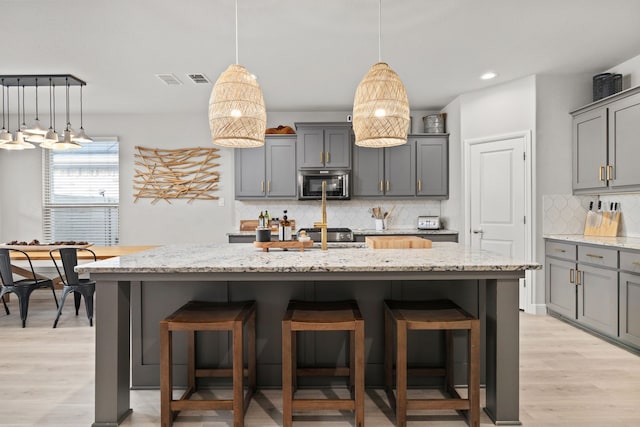 kitchen featuring a center island with sink, gray cabinetry, and light hardwood / wood-style flooring