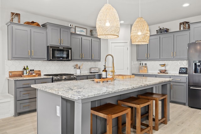 kitchen featuring appliances with stainless steel finishes, light wood-type flooring, a kitchen island with sink, and gray cabinetry