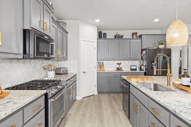 kitchen with appliances with stainless steel finishes, light wood-type flooring, tasteful backsplash, sink, and pendant lighting