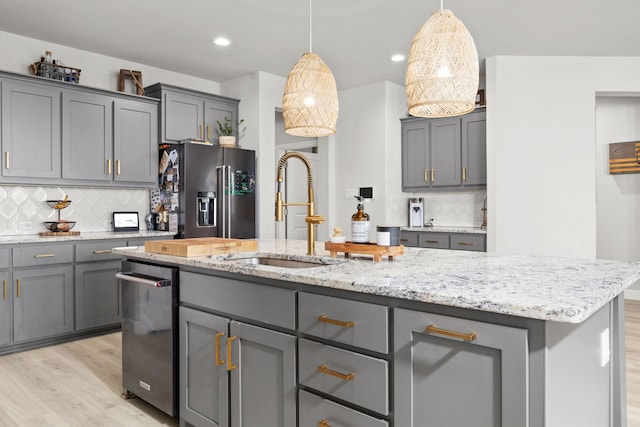 kitchen with gray cabinetry, a center island with sink, hanging light fixtures, and appliances with stainless steel finishes