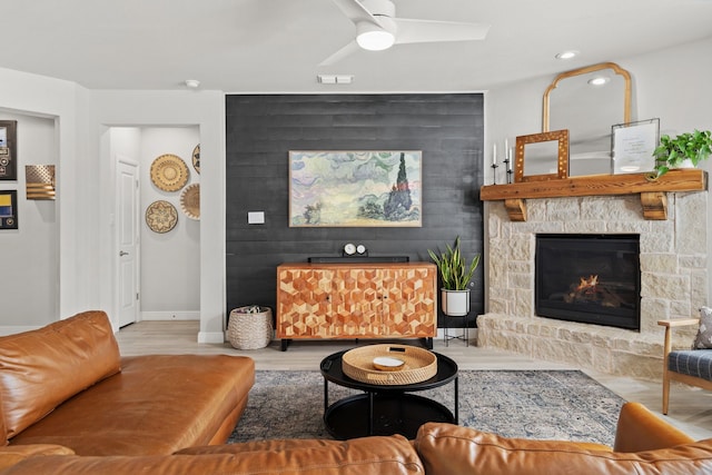 living room with a stone fireplace, ceiling fan, and light hardwood / wood-style flooring