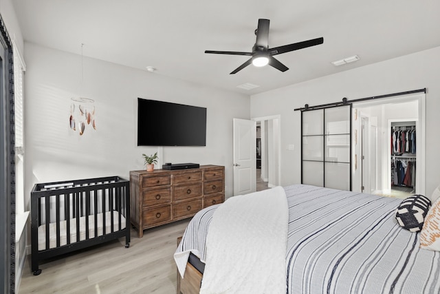 bedroom featuring a barn door, ceiling fan, a closet, and light hardwood / wood-style flooring