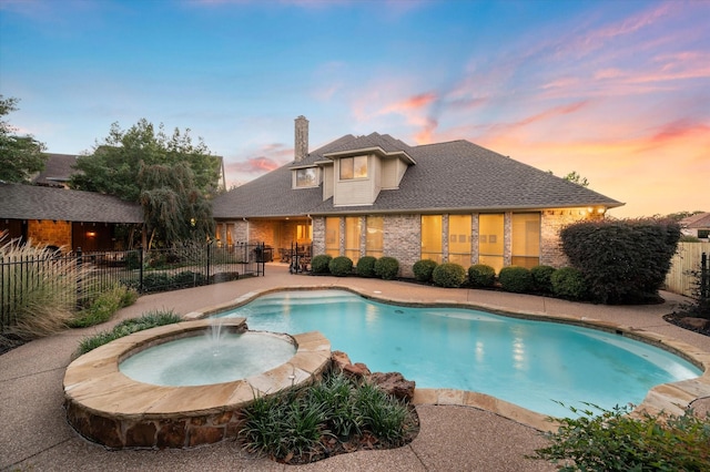 pool at dusk featuring pool water feature and an in ground hot tub