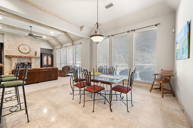 dining area featuring ceiling fan, vaulted ceiling with beams, and a fireplace