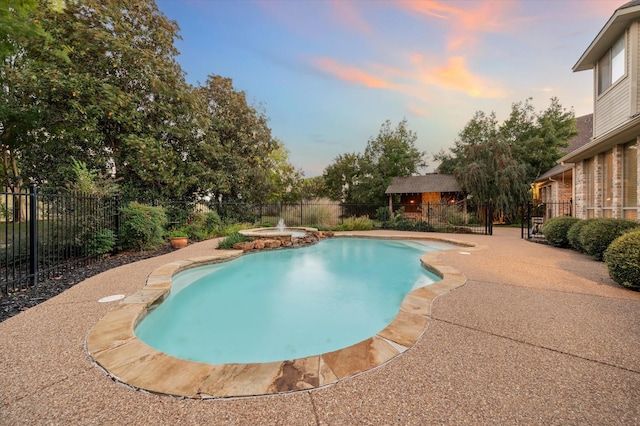 pool at dusk with an in ground hot tub and a patio area