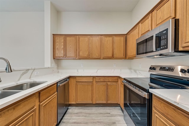 kitchen with appliances with stainless steel finishes, sink, light stone counters, and light hardwood / wood-style flooring