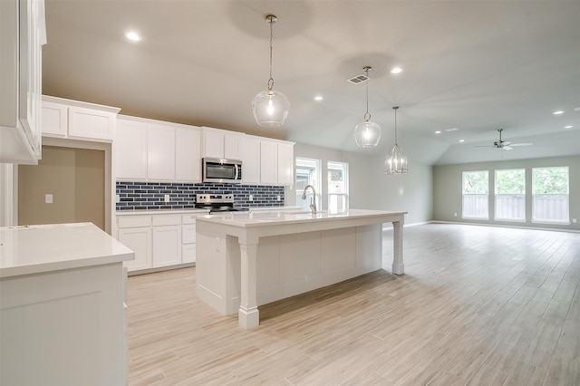 kitchen with stainless steel appliances, a center island with sink, light hardwood / wood-style flooring, white cabinetry, and lofted ceiling