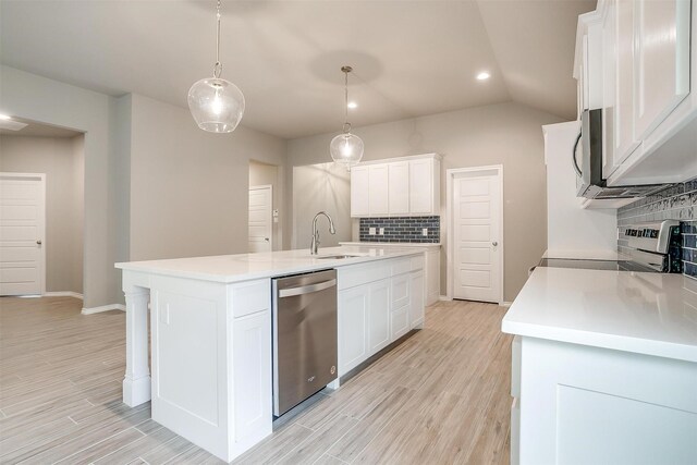 kitchen with appliances with stainless steel finishes, tasteful backsplash, hanging light fixtures, and an island with sink