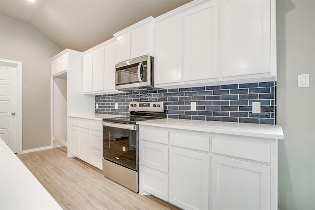 kitchen with backsplash, vaulted ceiling, light wood-type flooring, white cabinetry, and stainless steel appliances