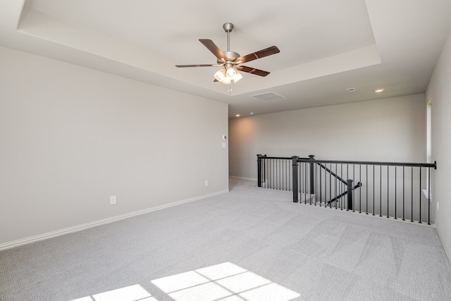 carpeted spare room with ceiling fan and a tray ceiling