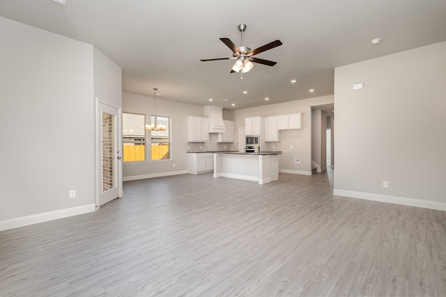 unfurnished living room with ceiling fan with notable chandelier and light wood-type flooring