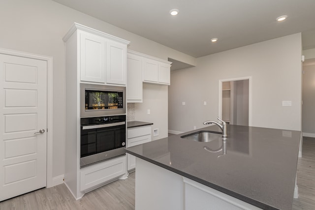 kitchen with stainless steel oven, light wood-type flooring, white cabinetry, and sink