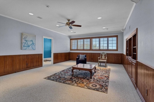 living room featuring light carpet, ceiling fan, ornamental molding, and wood walls