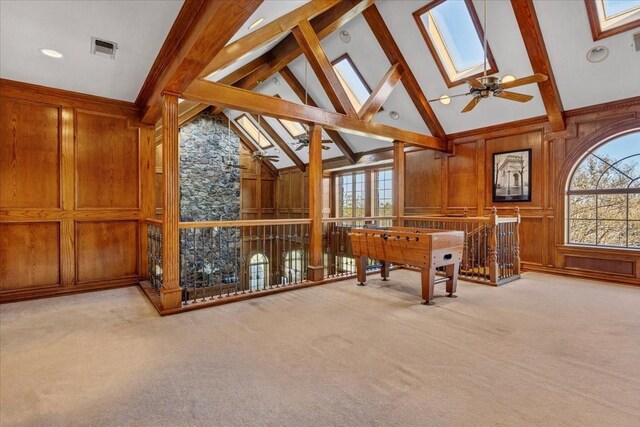 interior space featuring a skylight, wooden walls, beamed ceiling, high vaulted ceiling, and light carpet