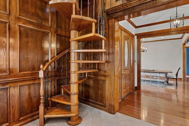 staircase with crown molding, wooden walls, a chandelier, and wood-type flooring