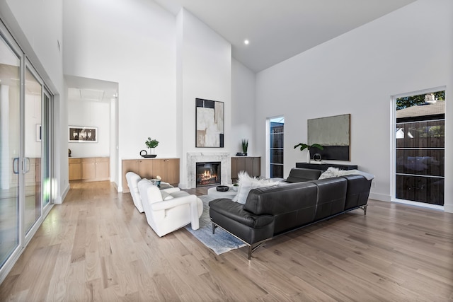 living room with a high end fireplace, light hardwood / wood-style floors, and high vaulted ceiling