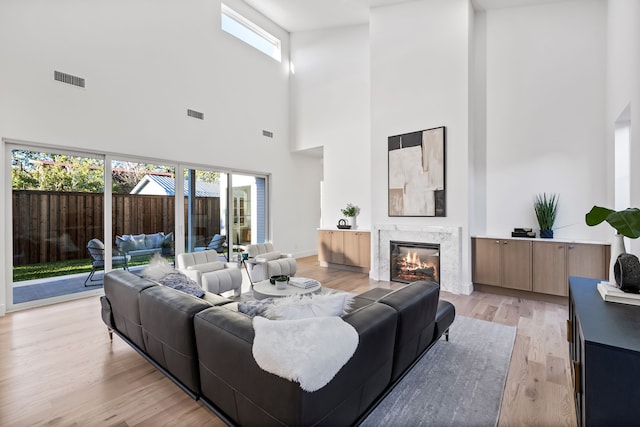 living room featuring a high end fireplace, light hardwood / wood-style floors, a towering ceiling, and a wealth of natural light