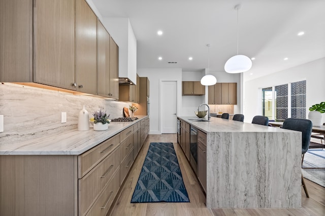 kitchen with sink, hanging light fixtures, light hardwood / wood-style flooring, tasteful backsplash, and light stone counters