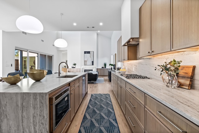 kitchen with sink, light stone counters, a large island with sink, light hardwood / wood-style floors, and decorative light fixtures