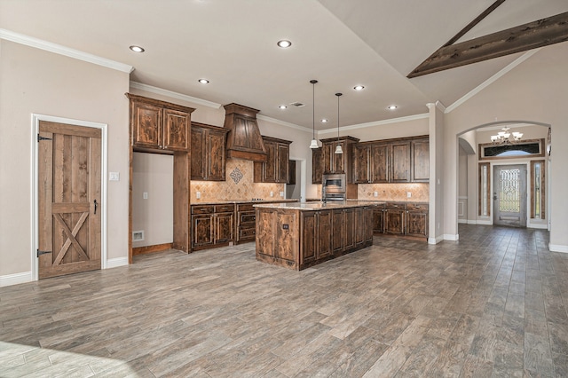 kitchen featuring hardwood / wood-style floors, backsplash, an island with sink, and hanging light fixtures