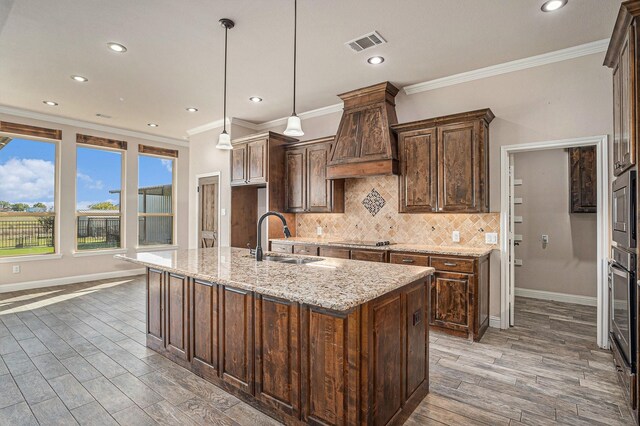 kitchen featuring sink, hanging light fixtures, light stone counters, dark hardwood / wood-style floors, and a center island with sink