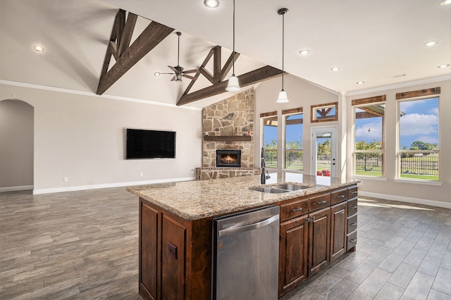 kitchen with a stone fireplace, sink, hanging light fixtures, stainless steel dishwasher, and an island with sink