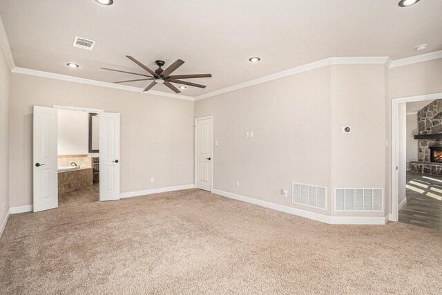 carpeted spare room with a stone fireplace, crown molding, and ceiling fan