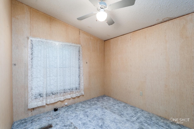 carpeted empty room with a textured ceiling, ceiling fan, and wood walls