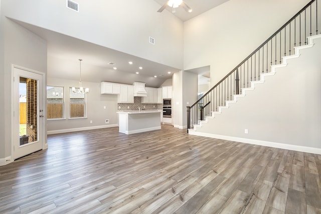 unfurnished living room featuring light hardwood / wood-style flooring, a towering ceiling, and ceiling fan with notable chandelier