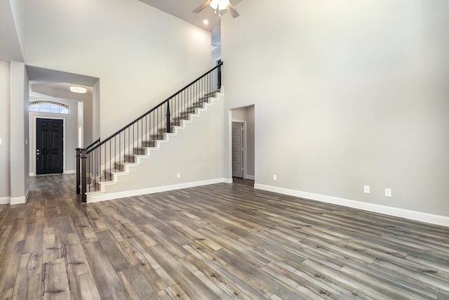 unfurnished living room featuring ceiling fan, a towering ceiling, and dark wood-type flooring