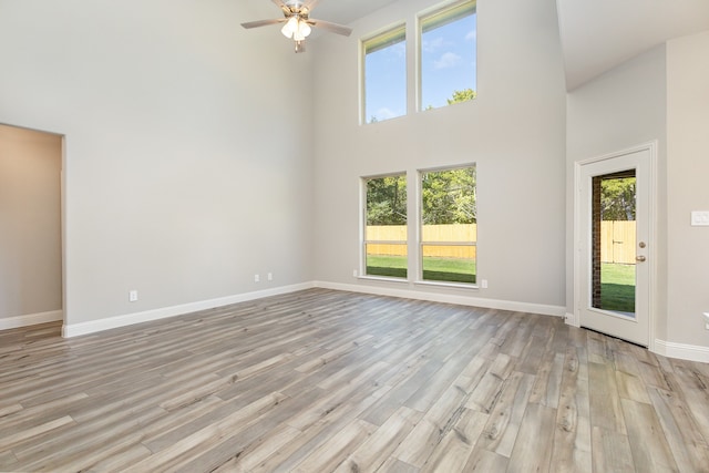 unfurnished living room with ceiling fan, a high ceiling, and light wood-type flooring