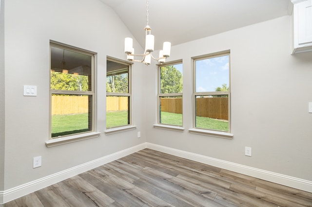 unfurnished dining area featuring a chandelier, light wood-type flooring, and vaulted ceiling