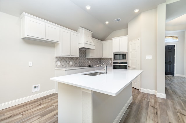 kitchen featuring black appliances, white cabinets, sink, light wood-type flooring, and an island with sink