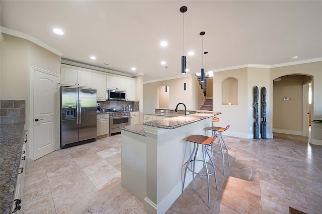 kitchen featuring stainless steel appliances, tasteful backsplash, a kitchen bar, white cabinets, and ornamental molding