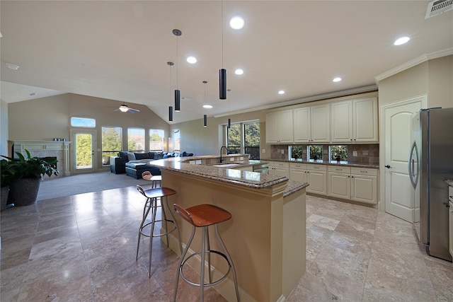 kitchen featuring ceiling fan, hanging light fixtures, backsplash, stainless steel fridge, and a center island with sink